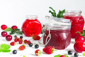 assortment of jams, seasonal fresh berries and fruits on white background