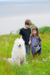 boy and girl in the summer with a big mount dog of the Samoyed