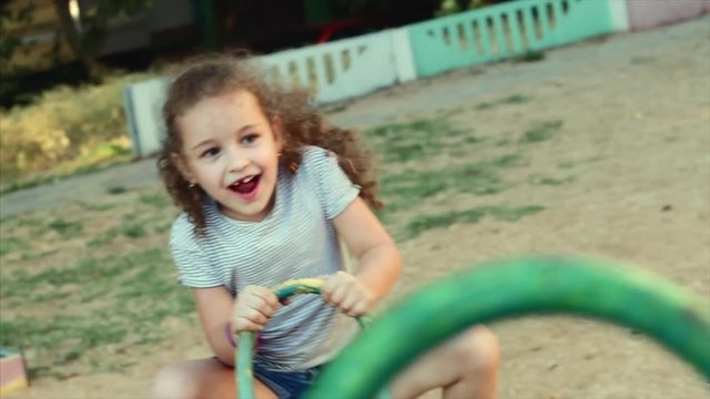 Happy young little girl spinning in a swing and smiling