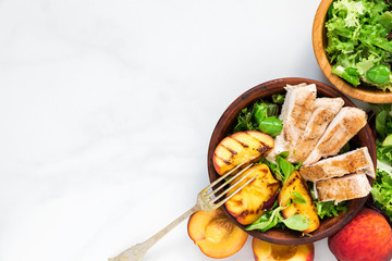 salad with grilled chicken and peach in a bowl with fork. healthy food. top view