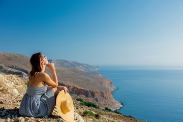 Young redhead girl in hat and dress with sea coastline on Balos, Crete, Greece