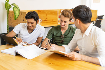 New employees taking corporate training for newcomers. Three young men writing notes at classroom...