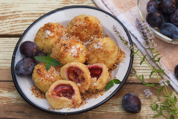 Typical Austrian plum dumplings made of leavened dough and fresh plums. Vintage wooden background decorated with mint flowers.