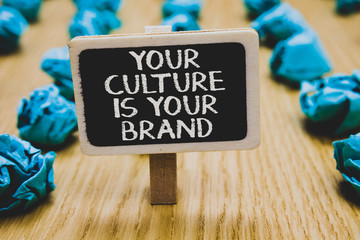 Handwriting text writing Your Culture Is Your Brand. Concept meaning Knowledge Experiences are a presentation card Stand blackboard with white words behind blurry blue paper lobs woody floor.