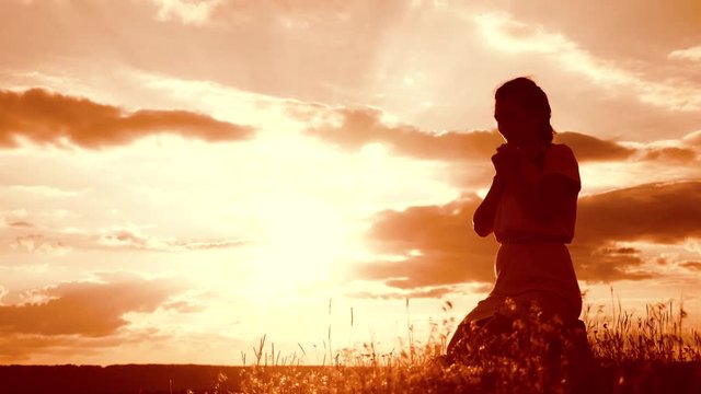 Girl folded her hands in prayer silhouette at sunset. woman praying on her knees. slow motion video. concept Christianity religion catholicism. Girl folded her hands in prayer pray to God. the girl