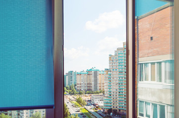 View on a dormitory district from an open window. Modern red brick building reflected in window. Blue blinds and blue sky outside. 