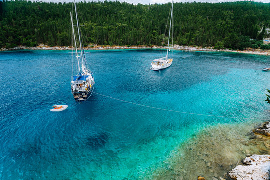 Crystal clear transparent blue turquoise teal mediterranean sea water of Foki Fiskardo Beach with some white yacht in the bay, Kefalonia, Ionian islands, Greece
