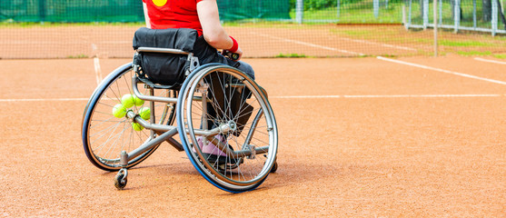 Disabled young woman on wheelchair playing tennis on tennis court.