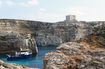 Fototapeta na wymiar Boat on the lagoon with high cliffs and Santa Marija Tower on Comino Island in Malta (Torri ta' Kemmuna)