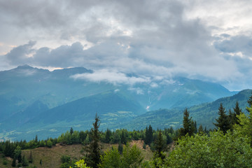 Svaneti mountain landscape with green grassy hills, snowy peaks and white clouds on summer day, Georgia