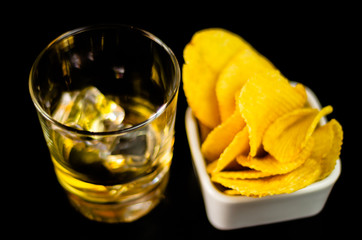 glass of whiskey with ice cubes and salty snacks on the background of the bar
