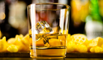 glass of whiskey with ice cubes and salty snacks on the background of the bar
