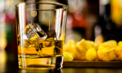 glass of whiskey with ice cubes and salty snacks on the background of the bar