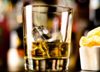 glass of whiskey with ice cubes and salty snacks on the background of the bar