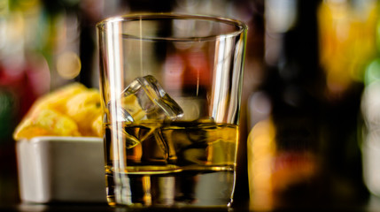 glass of whiskey with ice cubes and salty snacks on the background of the bar