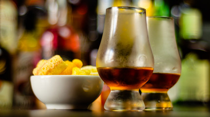 glass of whiskey with ice cubes and salty snacks on the background of the bar