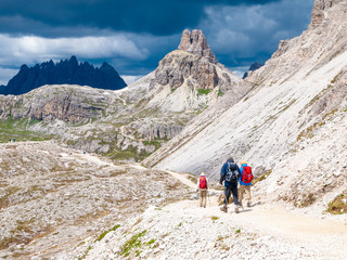 Fototapeta na wymiar Mountain hikers with trekking poles walks on the rocky path in the mountains. Nordic walking theme.