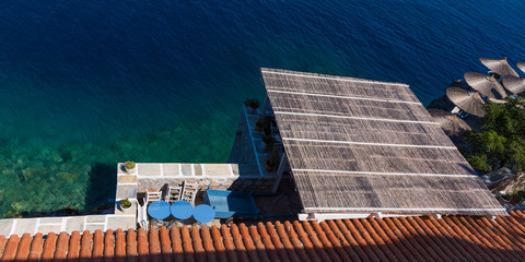 Arial view of square roof, round tables, terracotta slates and aquamarine sea 
