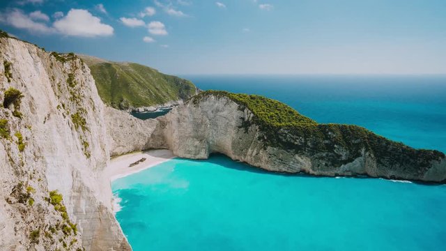 Timelapse of the world famous Navagio beach, Zakynthos, Greece. Turquoise sea water rolled to white sand beach with Shipwreck. Clouds moving in sky. Fist tourist boat arrived the bay
