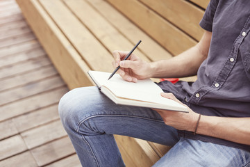 Close-up of mans hands writing in a note book sitting outside. Concept of education students youth.