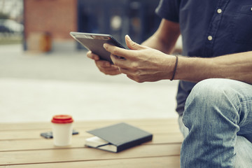 Man working outside in park using modern tablet, notebook, mobile phone. Close-up hands holding personal gadget.