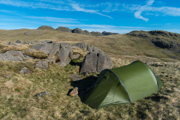 Green tent at Cold Pike in the Lake District, UK, overlooking the Crinkle Crags, Great Knott, Browney Gill and Oxendale on a bright hot summer morning with a footpath heading off in the distance.