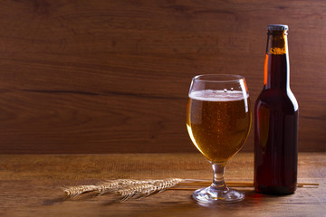 Glass and bottle of beer, ears of barley on wooden table. Ale. Room for text