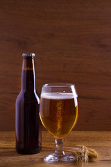 Glass and bottle of beer, ears of barley on wooden table. Ale. Room for text