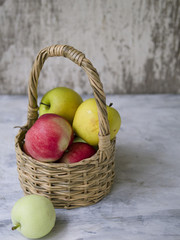 Basket with multi-colored apples (red, yellow, green) on a gray background. Close up