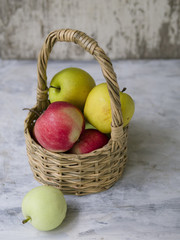 Basket with multi-colored apples (red, yellow, green) on a gray background. Close up