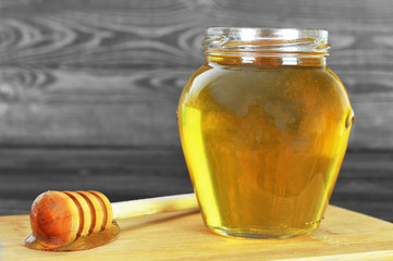 Honey jar with honey dipper on wooden background