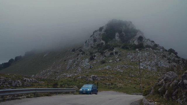 A car parked on a hill in front of a cloud covered mountain