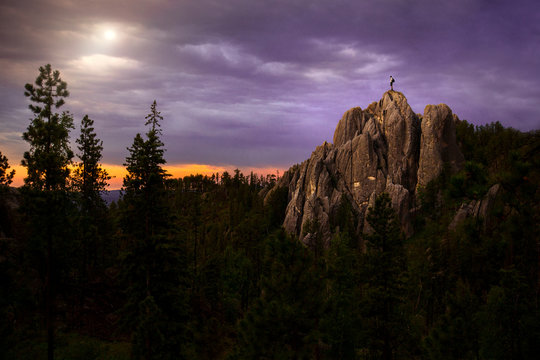 Climber Standing On Rocky Formation In Black Hills Top With A Gorgeous Landscape View Of A Forest Sunset 