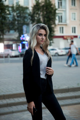 Fototapeta na wymiar Girl in black trousers and jacket.The blonde in the black suit.Blonde posing in the city