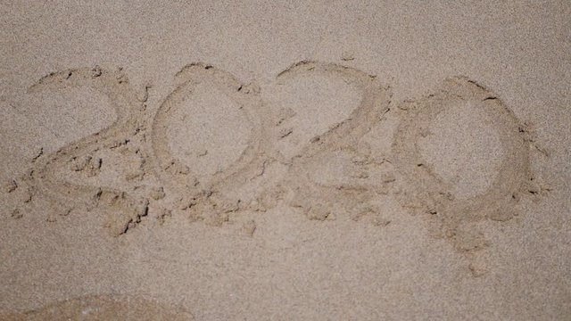 New year 2020 handwritten is appearing after wahing away 2019 y on sandy beach.