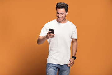 Smiling handsome man with mobile phone on yellow background.