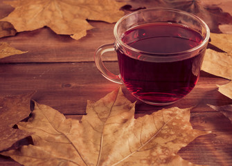 Autumn still life cup with red tea on maple leaves on a wooden table.