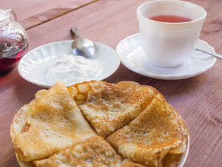 Karkade tea in a white cup with saucer and pancakes with sour cream on a wooden background