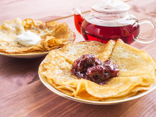 Pancakes on plates. With jam and sour cream. Teapot with tea.