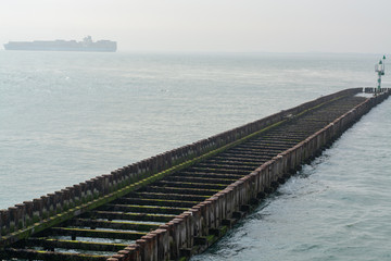 Sea near Vlissingen, Zeeland, Netherlands, old wooden pier at high tide and big cargo ship on horizon