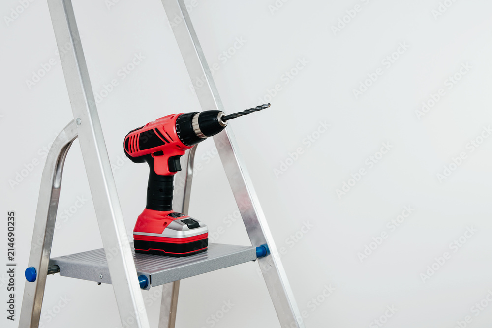 Poster view of the screwdriver. a red cordless screwdriver is placed on the ladder. necessary tools at home