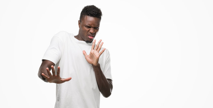 Young african american man wearing white t-shirt disgusted expression, displeased and fearful doing disgust face because aversion reaction. With hands raised. Annoying concept.