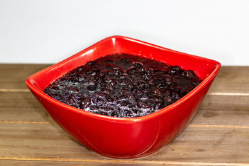 Red bowl filled with black bean soup ready to eat on the kitchen table