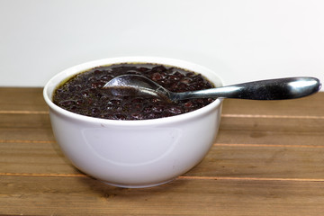 White bowl filled with black bean soup and a spoon ready to eat on the kitchen table