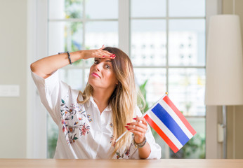 Young woman at home holding flag of Thailand stressed with hand on head, shocked with shame and surprise face, angry and frustrated. Fear and upset for mistake.