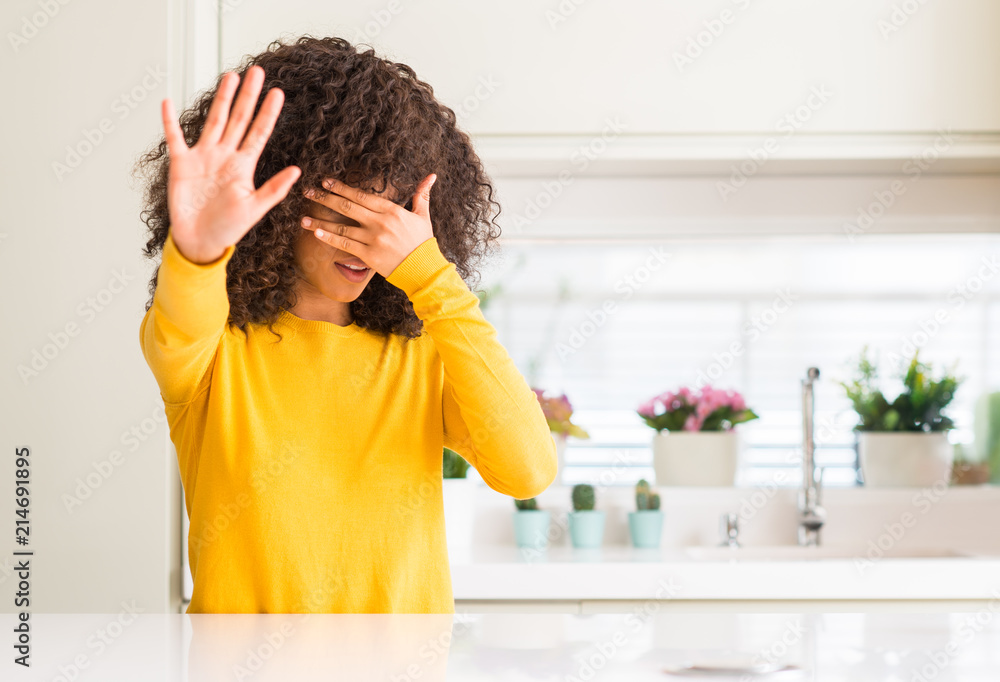 Sticker African american woman wearing yellow sweater at kitchen covering eyes with hands and doing stop gesture with sad and fear expression. Embarrassed and negative concept.