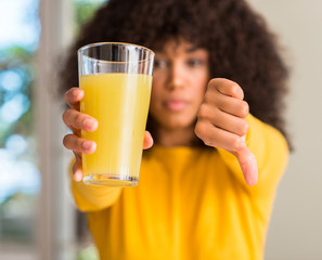 African american woman drinking healthy fruit juice at home with angry face, negative sign showing...