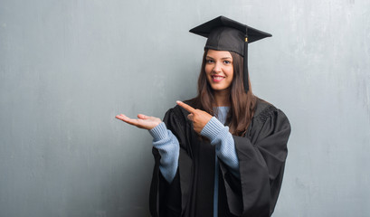 Young brunette woman over grunge grey wall wearing graduate uniform very happy pointing with hand...