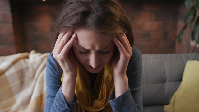 Face of young woman with a headache sitting in home on sofa feel ill unhappy ache adult female symptom health unhealthy young infection pills medicine portrait