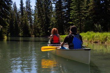 Couple adventurous friends are canoeing in a river surrounded by the Canadian nature. Taken in Vermilion Lakes, Banff, Alberta, Canada.